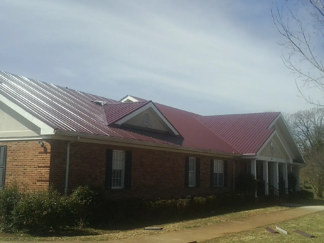 Red metal roof with gabled entries on a long brick building, from a Hail Damage Roof Repair job in Rockwood