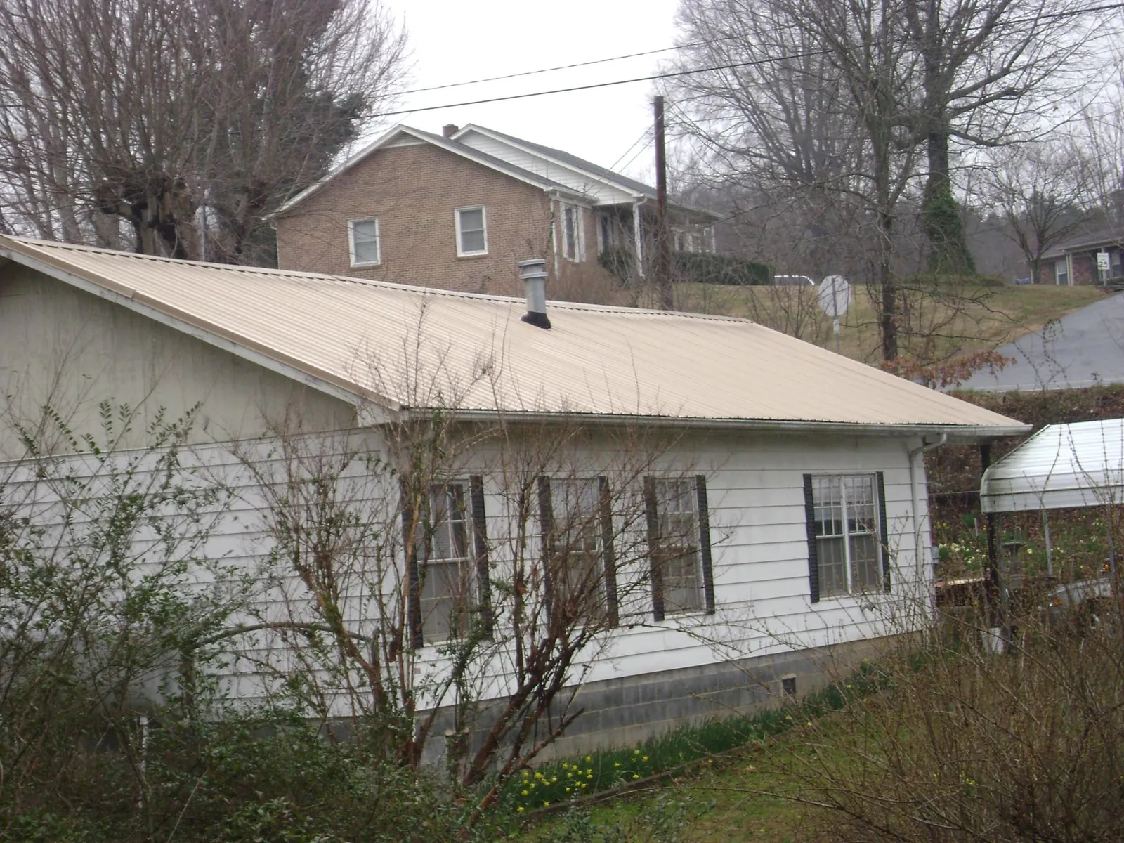 Tan metal roof on a white sided house set into a hillside — Commercial Roofing by Roofing Brothers in Rockwood